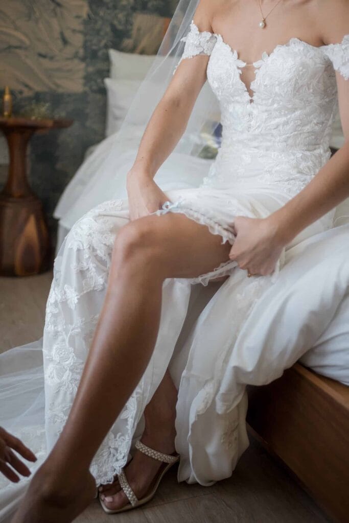 Bride sitting on a bed, adjusting her lace wedding dress and garter, preparing for the wedding ceremony in an intimate and elegant setting